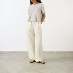 Model wearing Lisa Yang Liru Cashmere T-Shirt in Seashell, styled with cream wide-leg trousers and black flat sandals.