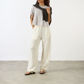 Model wearing Lisa Yang Liru Cashmere T-Shirt in Seashell, styled with cream wide-leg trousers, dark scarf and sandals.
