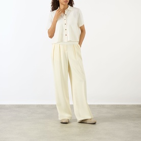 Model wearing Lisa Yang cream cashmere short-sleeve polo top with button placket, styled with wide-leg cream trousers and flat shoes.