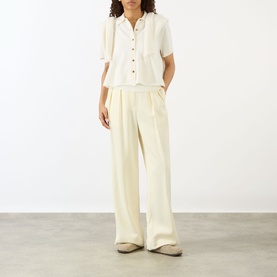 Model wearing Lisa Yang cream cashmere short-sleeve shirt with button placket and chest pocket, styled with matching wide-leg trousers