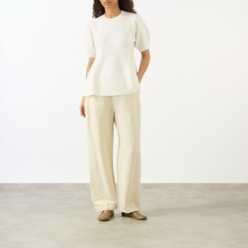 Model wearing Lisa Yang The Mella Peplum Top in Cream, crew neck, short sleeves, peplum hem, styled with wide-leg trousers and loafers.