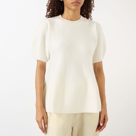 Model wearing Lisa Yang The Mella Peplum Top in cream, featuring crew neck, sheer short sleeves and knit structure, styled with beige trousers