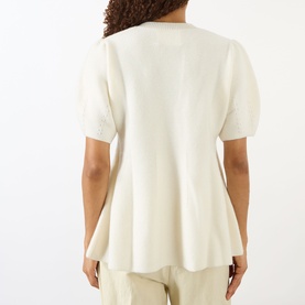 Model wearing Lisa Yang The Mella Peplum Top in cream, showing back view with short sleeves and peplum hem, styled with cream trousers.