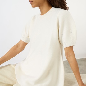 Model wearing Lisa Yang The Mella Peplum Top in cream, featuring crew neckline, short puff sleeves and knit structure, styled with beige trousers.