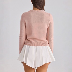 Model wearing House of CB white knit sweater, back view, styled with white pleated mini shorts