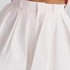 Model wearing House of CB white wide-leg tailored trousers with pleated front detail and belt loops, close-up view
