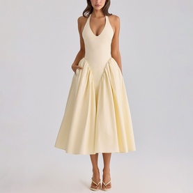 Model wearing a pale yellow halterneck midi dress with deep V-neckline, full pleated skirt and side pockets, styled with strappy heeled sandals