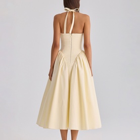 Model wearing a pale yellow halterneck midi dress with structured bodice, tie-neck detail, and full pleated skirt, shot from behind