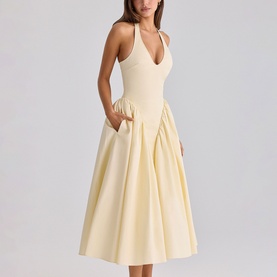 Model wearing a pale yellow halterneck midi dress with deep V-neckline, pleated full skirt, and side pockets
