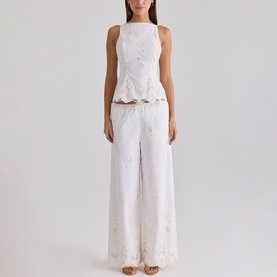 Model wearing House of CB white wide-leg trousers with floral broderie detail, styled with matching sleeveless peplum top