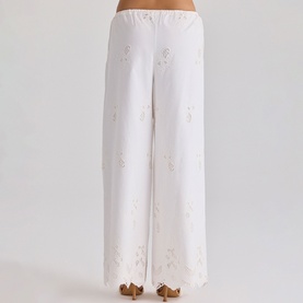 Model wearing House of CB white wide-leg trousers with floral embroidery and scalloped hem, shown from behind