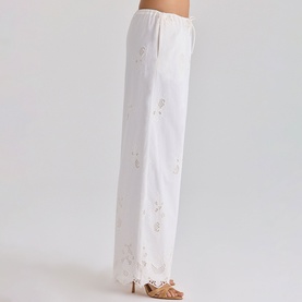 Model wearing House of CB white wide-leg trousers with floral cutwork embroidery, styled with strappy heeled sandals