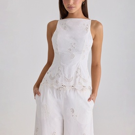 Model wearing House of CB white sleeveless top with floral cutwork embroidery, styled with matching white wide-leg trousers