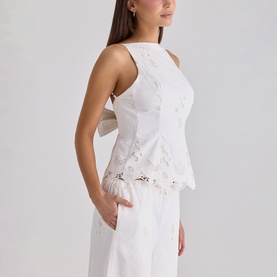 Model wearing House of CB white sleeveless peplum top with broderie anglaise detailing and scalloped hem, styled with white wide-leg trousers