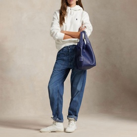 Model carrying a blue shoulder bag, wearing Polo Ralph Lauren white hoodie, blue jeans and white trainers