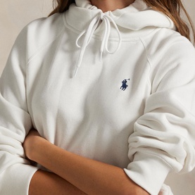 Model wearing Polo Ralph Lauren white fleece hoodie with navy embroidered pony logo, drawstring hood, arms crossed.