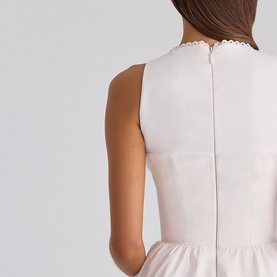 Model wearing House of CB white sleeveless dress, back view showing zip fastening and scallop-edged neckline detail