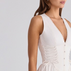 Model wearing House of CB white sleeveless dress with deep V-neckline, pearl button detail, and corset lace-up front panel.