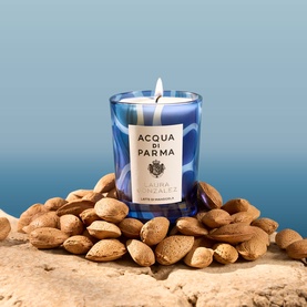 Acqua Di Parma Luna Gonzales scented candle in blue glass jar, lit flame, surrounded by almonds on stone surface