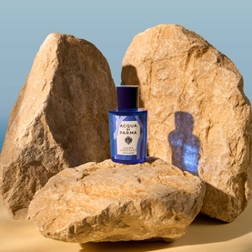 Acqua Di Parma blue EDT bottle displayed on sun-warmed sandstone rocks against a soft blue sky backdrop.