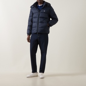 Model wearing Calvin Klein Jeans Dark Sapphire hooded puffer jacket, styled with matching navy trousers and white trainers.