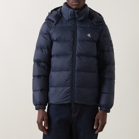 Model wearing Calvin Klein Jeans Dark Sapphire quilted hooded puffer jacket with logo badge, styled with dark jeans.