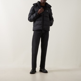 Model wearing Calvin Klein Jeans black quilted puffer jacket with hood, styled with dark trousers and black leather shoes.