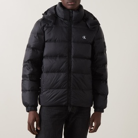 Model wearing Calvin Klein Jeans black hooded puffer jacket with quilted panels and logo badge on chest.