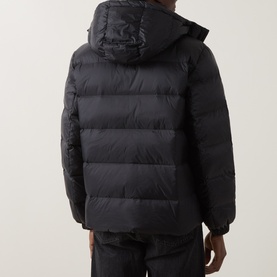 Model wearing Calvin Klein Jeans black hooded puffer jacket, rear view, with quilted panels and matching black trousers.
