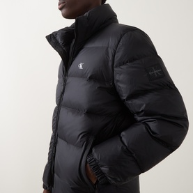 Model wearing Calvin Klein Jeans black puffer jacket with funnel neck, quilted panels and logo badge detail.