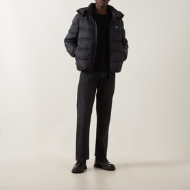 Model wearing Calvin Klein Jeans black puffer casual jacket with hood, styled with black trousers and leather shoes.