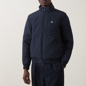 Model wearing Calvin Klein Jeans Dark Sapphire nylon casual jacket with zip front, ribbed hem, and logo badge, styled with navy trousers.