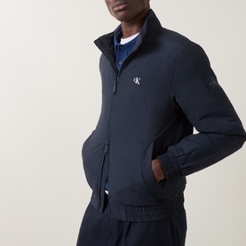 Model wearing Calvin Klein Jeans Dark Sapphire nylon casual jacket with funnel neck, zip front, and CK logo badge, styled with matching trousers.