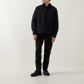 Model wearing Calvin Klein Jeans Back Graphic Padded Overshirt in black, styled with black trousers and chunky leather shoes.