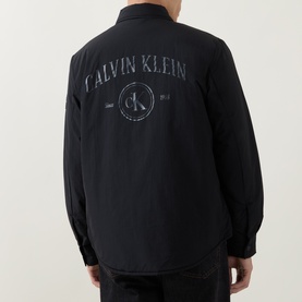 Model wearing Calvin Klein Jeans Back Graphic Padded Overshirt in black, rear view showing tonal circular logo graphic print.