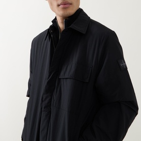 Model wearing Calvin Klein Jeans Back Graphic Padded Overshirt in black, showing point collar, concealed placket, and logo badge on sleeve.