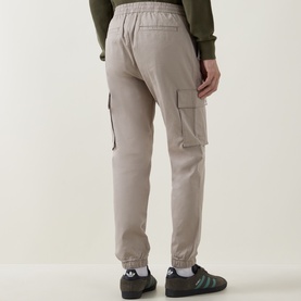Model wearing Calvin Klein Jeans Comfort Skinny Leg Cargo Trousers in Vintage Khaki, cuffed ankles, cargo pockets, styled with green trainers.