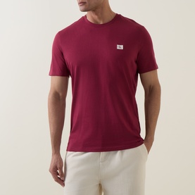Model wearing Calvin Klein Jeans Rhododendron cotton crew neck T-shirt with small chest logo patch, styled with light grey trousers.