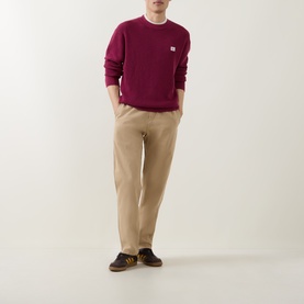 Model wearing Calvin Klein Jeans Badge Logo Waffle-Knit Sweatshirt in Rhododendron, styled with beige chinos and dark sneakers.