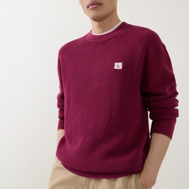 Model wearing Calvin Klein Jeans Badge Logo Waffle-Knit Sweatshirt in Rhododendron, crew neck with chest badge logo, styled with beige trousers.