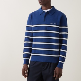 Model wearing blue and white striped long-sleeve knit polo shirt with embroidered chest logo, styled with navy trousers.