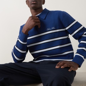 Model wearing blue and white striped Calvin Klein knit polo top with embroidered logo, styled with navy trousers