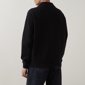 Model wearing black long-sleeve polo sweatshirt, rear view, styled with dark navy jeans