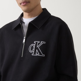 Model wearing black Calvin Klein quarter-zip sweatshirt with oversized CK monogram logo embroidery on chest