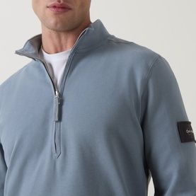 Model wearing Calvin Klein Jeans Steel Gray quarter-zip sweatshirt with silver zip and sleeve badge logo, styled over white tee.