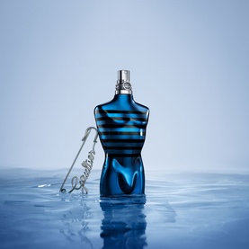 Jean Paul Gaultier Ultra Male EDP in iconic torso-shaped bottle, deep blue with black stripe design, emerging from water with silver safety pin detail