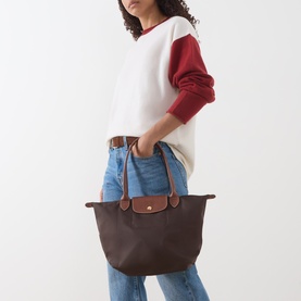 Model carrying Longchamp Le Pliage shoulder bag in Moka with tan leather trims, styled with white and red sweater and blue jeans.