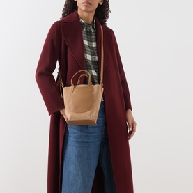 Model carrying Longchamp Complice XS Suede Crossbody Bag in Pecan with gold-tone hardware and adjustable strap, styled with burgundy coat and jeans