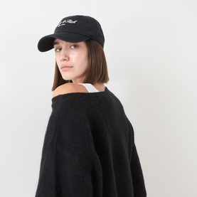Model with Sporty and Rich Faded Black cotton baseball cap, worn with black oversized knit sweater and white top underneath.