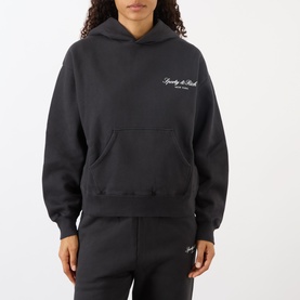 Model wearing Sporty and Rich Signature Logo Hoodie in Faded Black with matching sweatpants, featuring chest logo and kangaroo pocket.